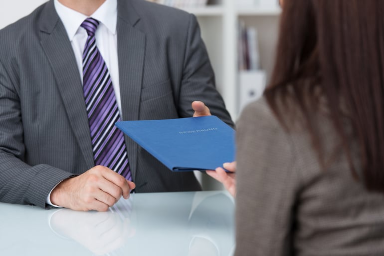 Employment interview with a close up view of a female applicant handing over a file containing her curriculum vitae to the businessman conducting the interview-2