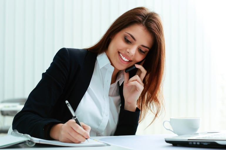 Young happy businesswoman talking on the phone and writing notes in office.jpeg